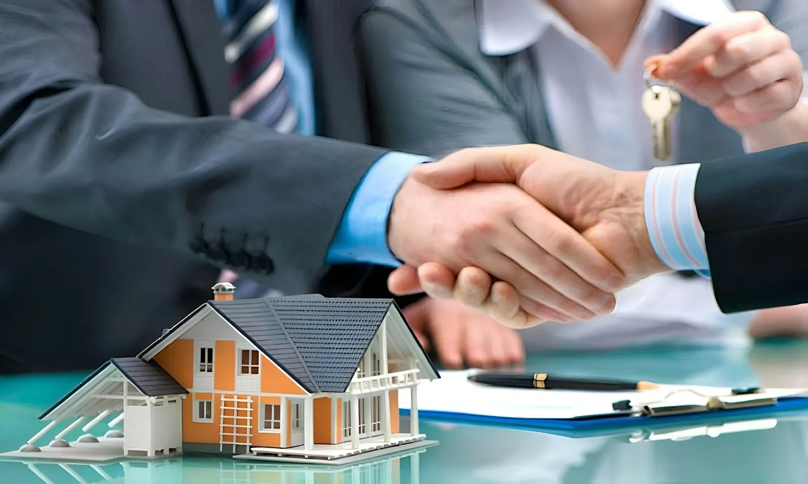 Two people shaking hands over a model house and keys after agreeing a deal