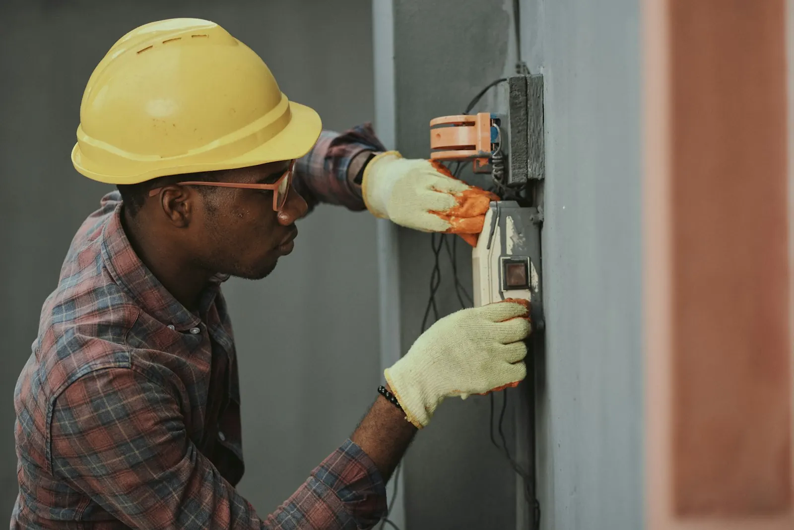 An electrician in a hard hat testing a meter box
