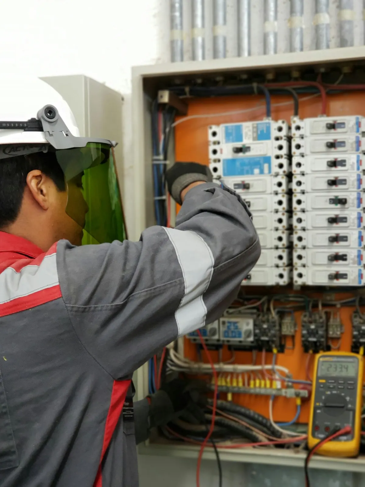 An electrician working on an open electrical panel with a meter