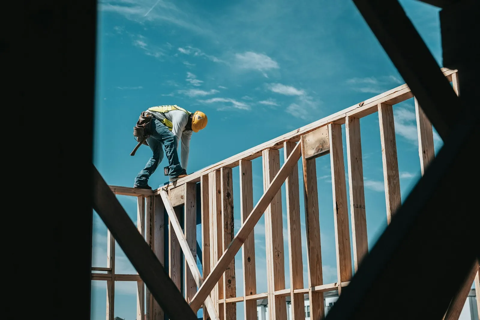 A framing carpenter standing on top of a wall frame against a blue sky
