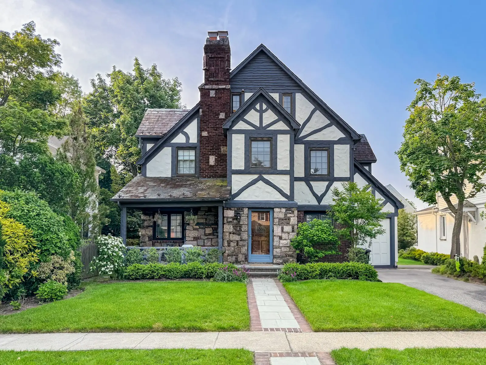 A tudor style home with a stone chimney and a neat lawn