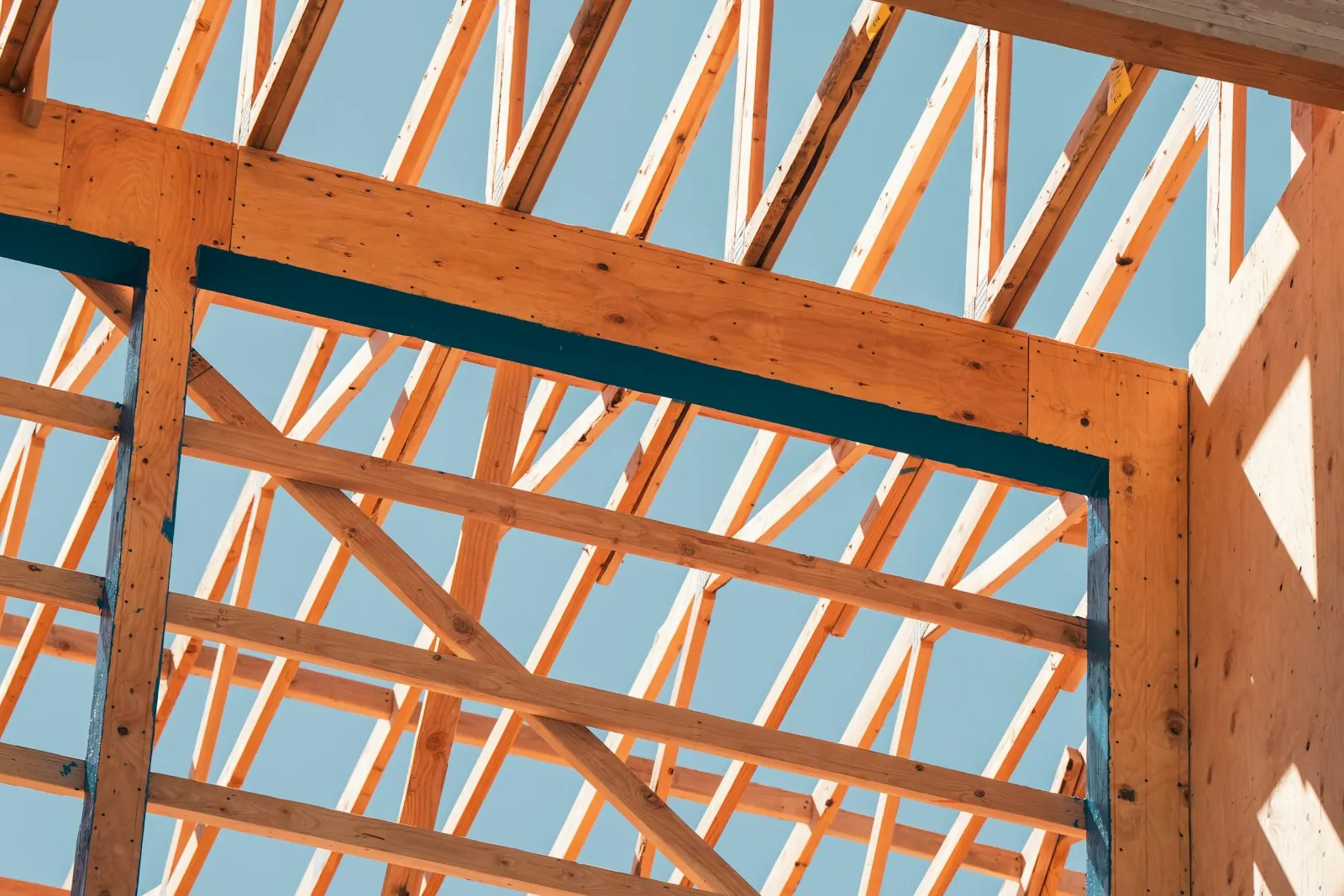 Wood roof trusses and beams framing a new house against a clear sky