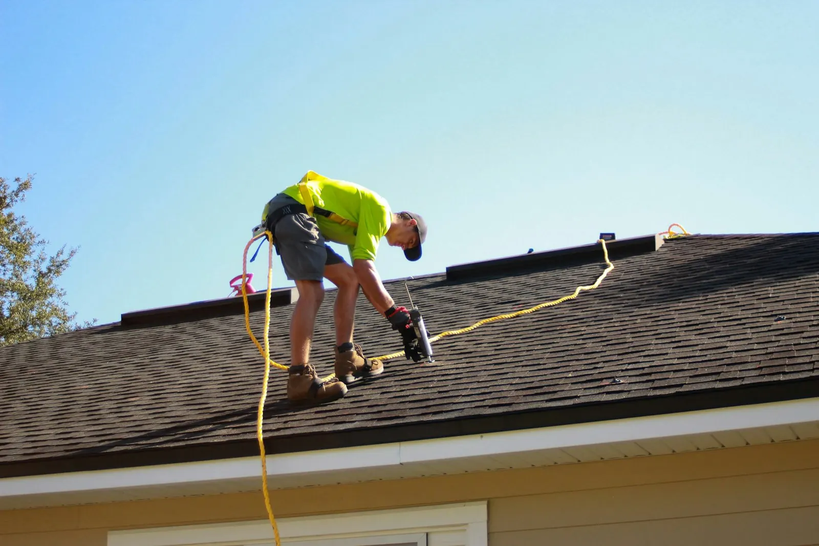 A roofer in a safety harness installing shingles on a residential roof