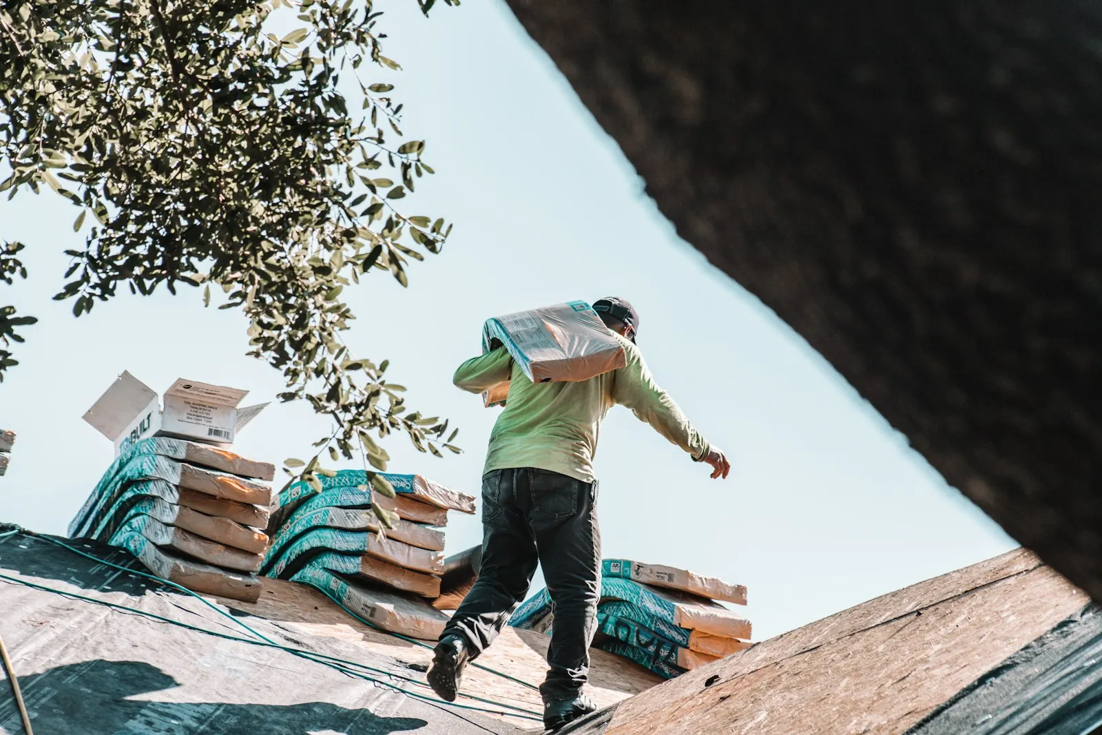 A roofer carrying a bundle of shingles across a roof