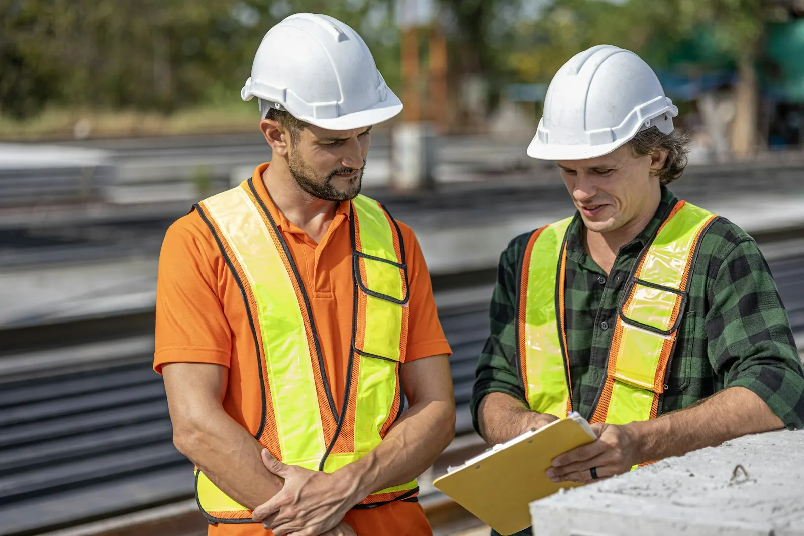 Two workers in hard hats and safety vests reviewing plans on a job site